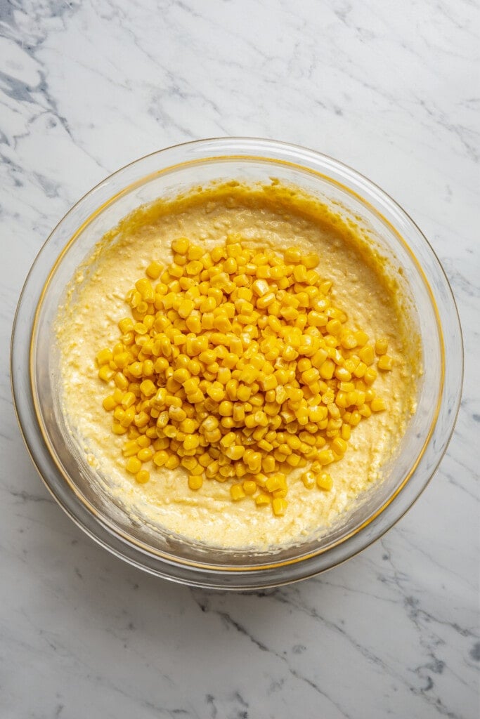 Adding whole corn kernels to cornbread casserole batter.