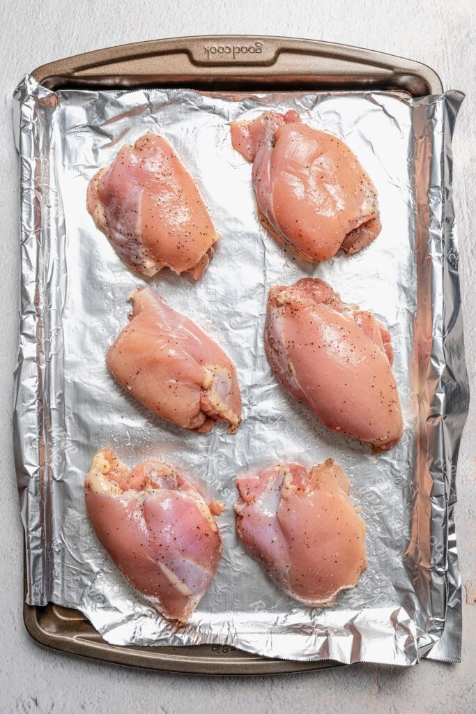 Raw, seasoned chicken thighs on a sheet pan lined with aluminum foil.