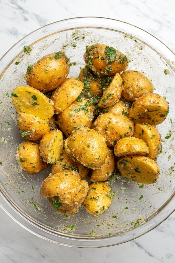Tossing scored potatoes in a garlic-butter sauce with parsley and parmesan.