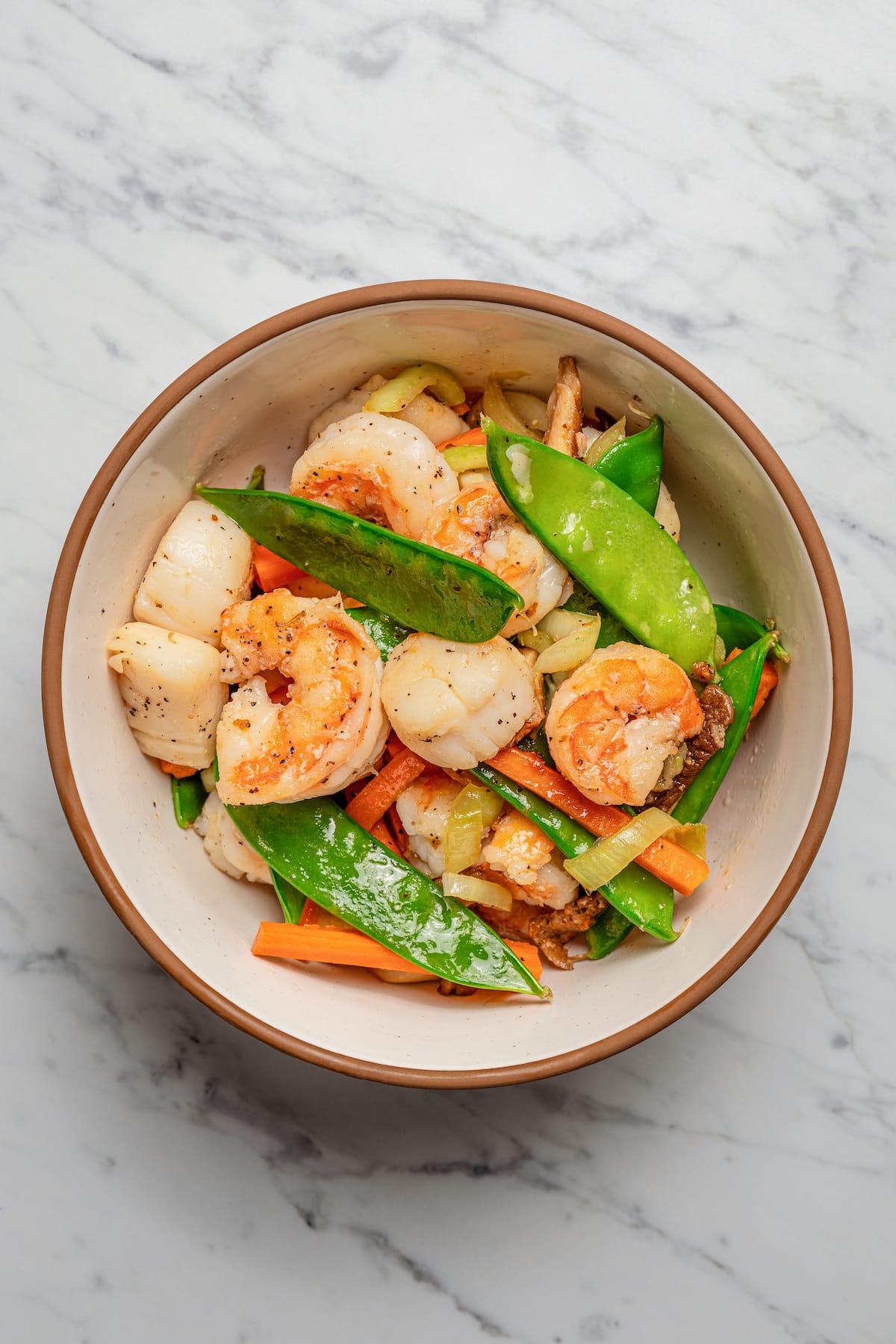 Adding stir-fried veggies and seafood to a bowl.