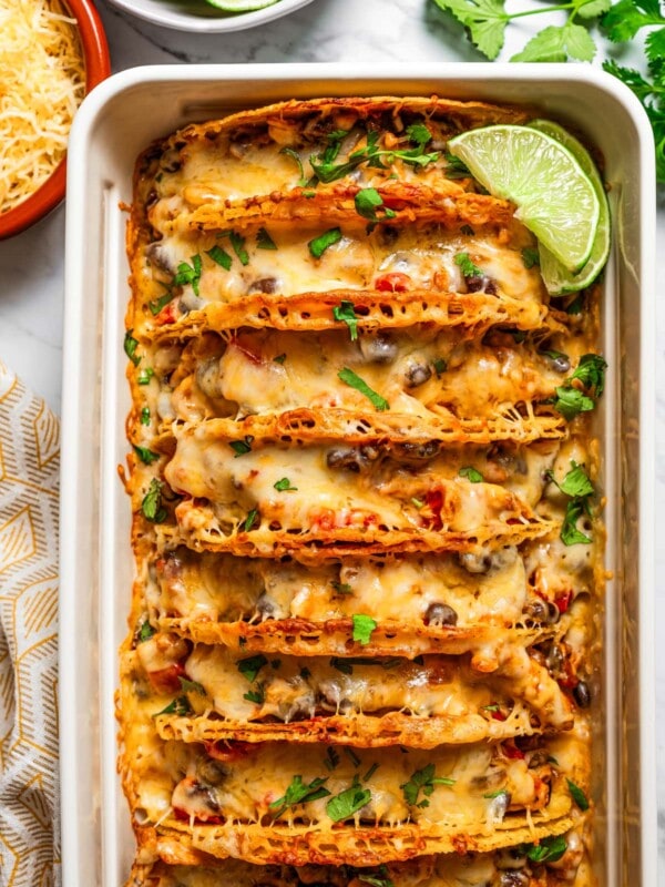 Overhead image of baked chicken tacos in a baking dish, and they are garnished with fresh cilantro and lime slices.