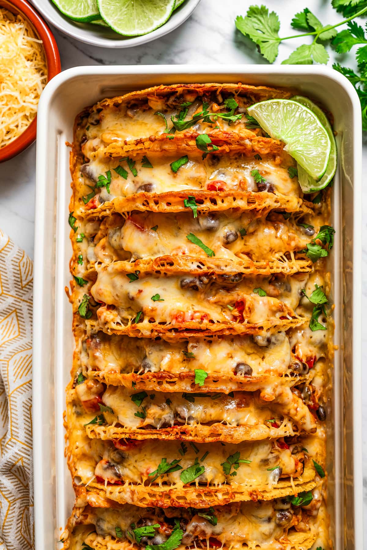 Overhead image of baked chicken tacos in a baking dish, and they are garnished with fresh cilantro and lime slices.