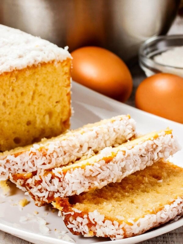 Banana pound cake topped with coconut flakes, arranged on a white platter, and partially sliced.