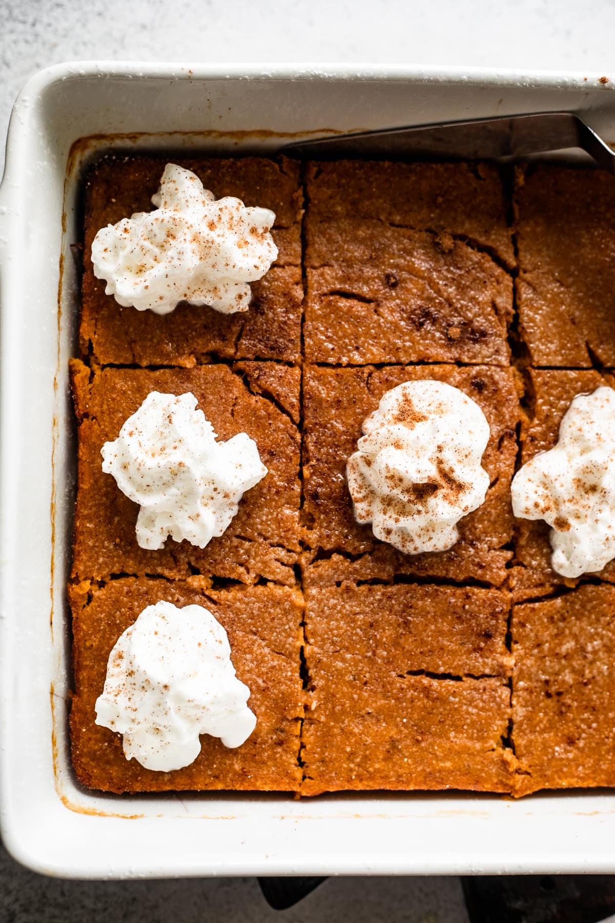 A square baking dish with pumpkin bars in it, topped with a swirl of whipped cream.