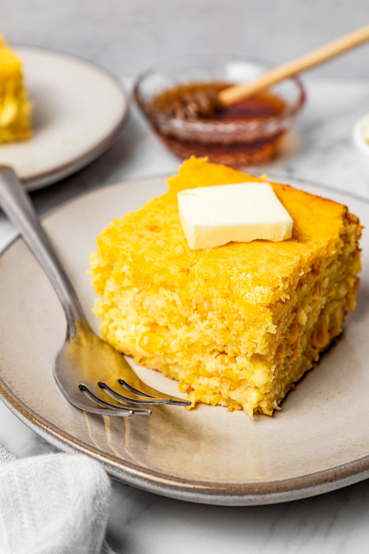 Cornbread Casserole A slice of cornbread casserole on a plate with a pad of butter on top.