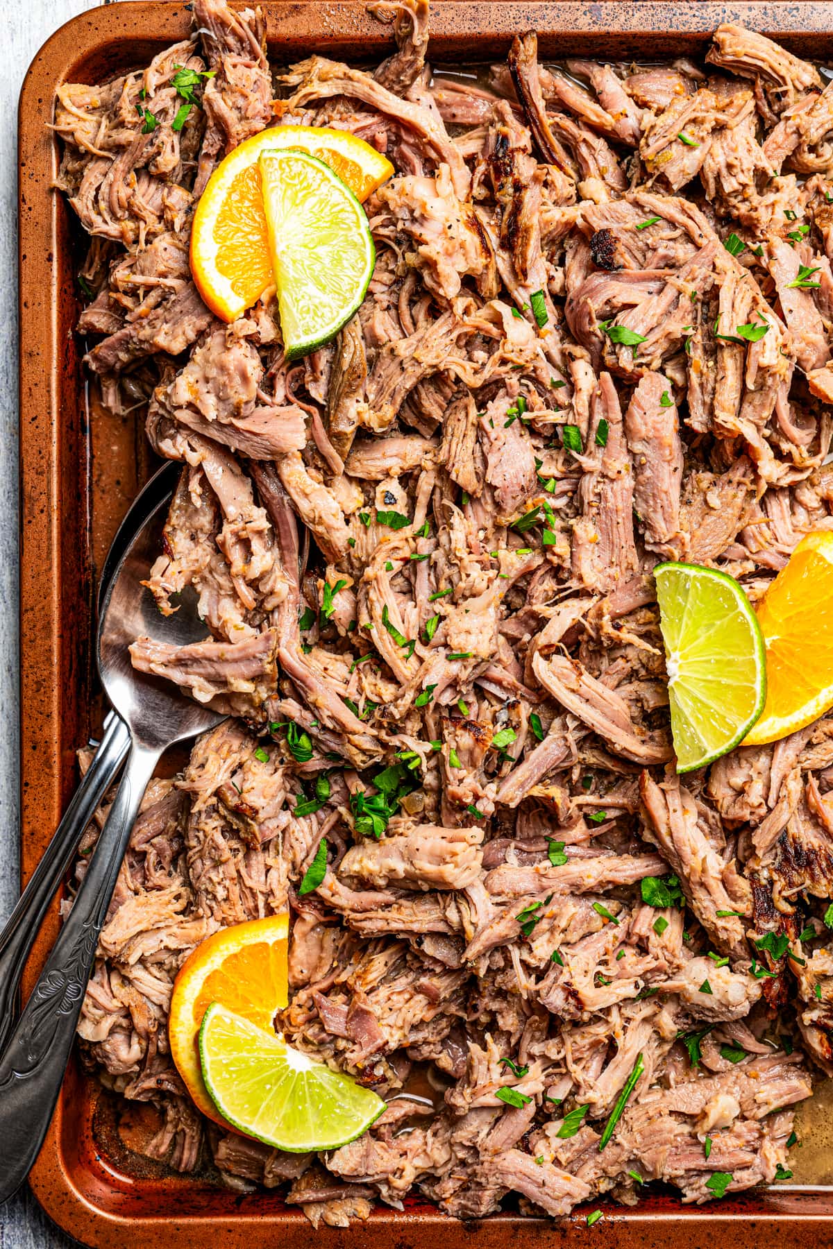Shredded Mojo Pork on a sheet pan with serving utensils set on top of the meat.