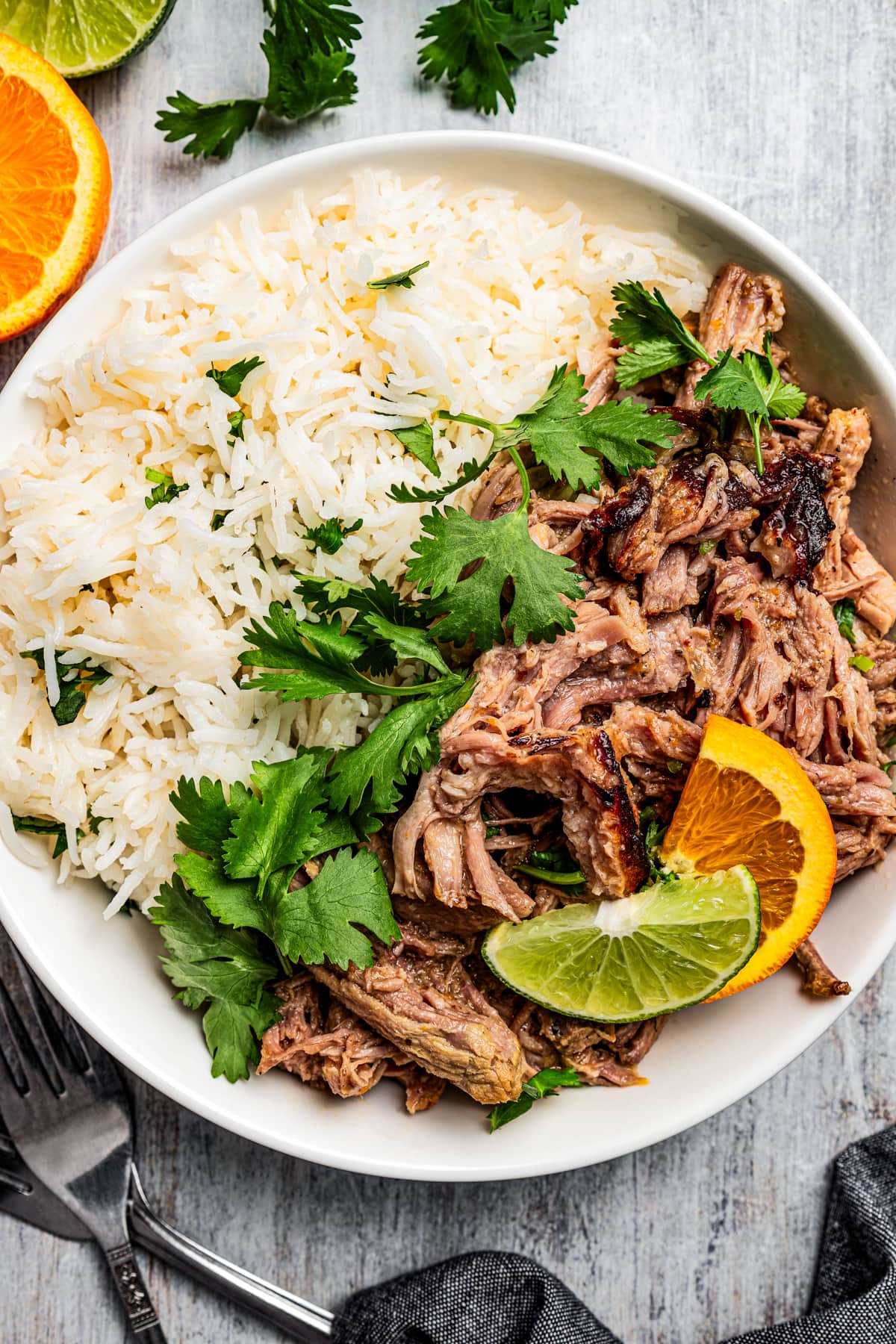 Overhead image of a dinner plate full of rice and mojo pork garnished with cilantro and orange slices.