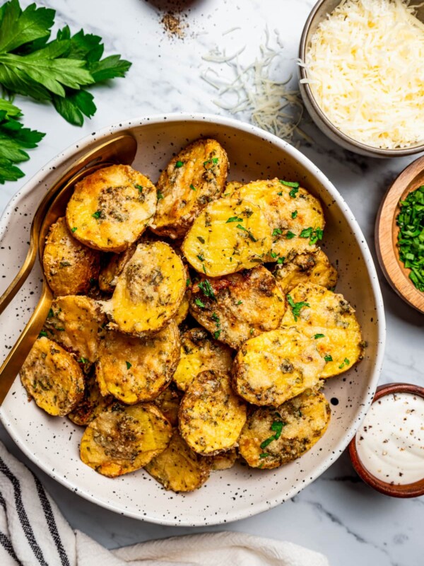 Overhead image of parmesan potatoes served in a bowl, with a bowl of parmesan cheese set next to the potatoes.