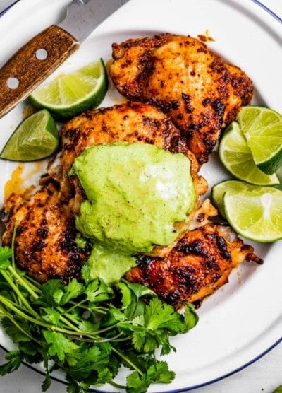 Peruvian chicken thighs served on a dinner plate and topped with a green sauce.