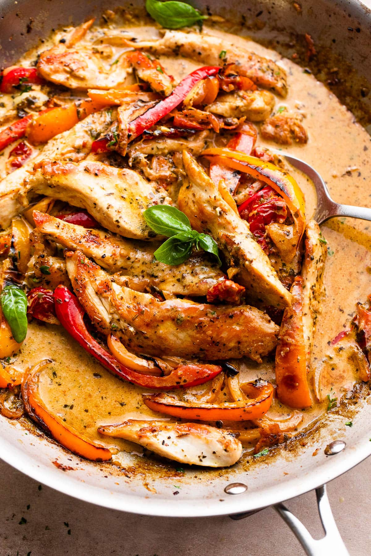 Sliced chicken and peppers in a creamy sauce cooking in a skillet.
