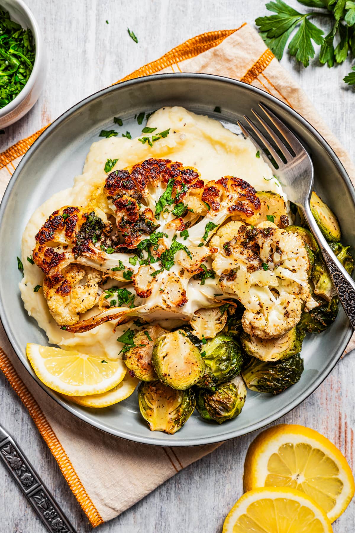 Roasted cauliflower steak served on a plate over mashed potatoes with brussels sprouts.