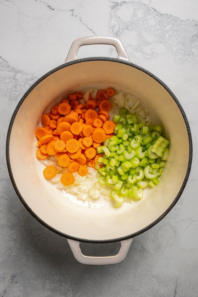 Adding carrots and celery to sauteed onions and garlic in a soup pot.