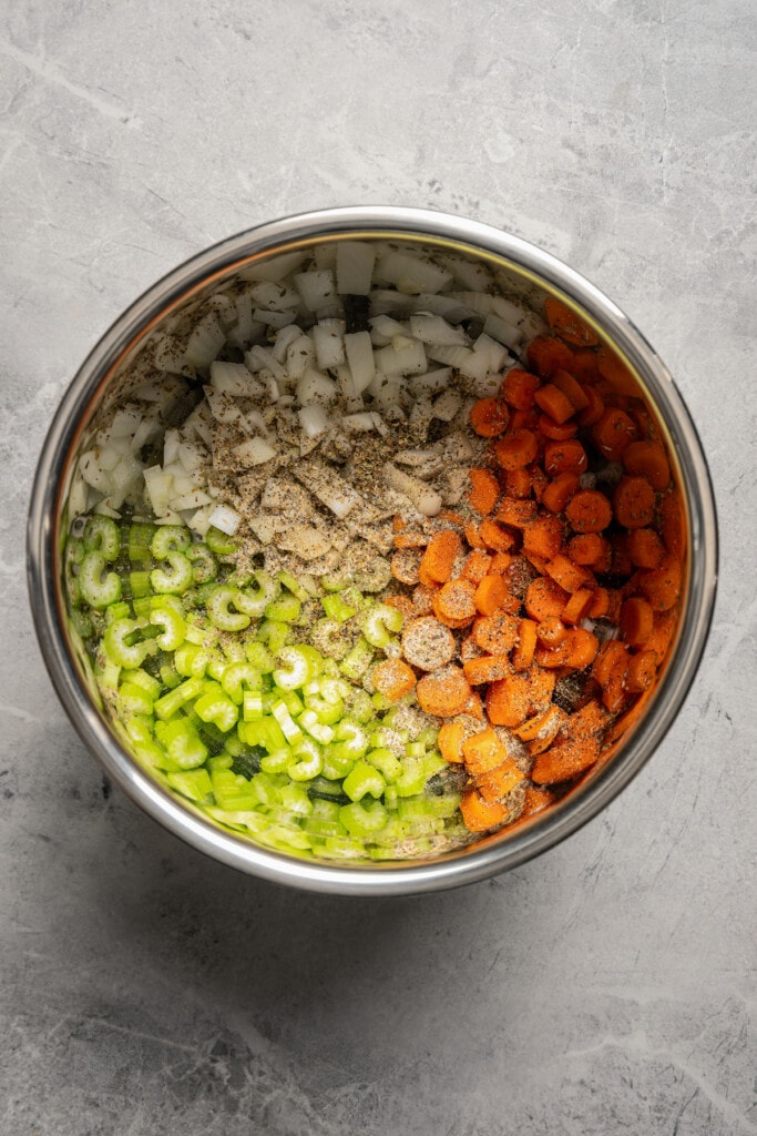 Adding onions, celery, carrots, and seasoning to an Instant Pot.