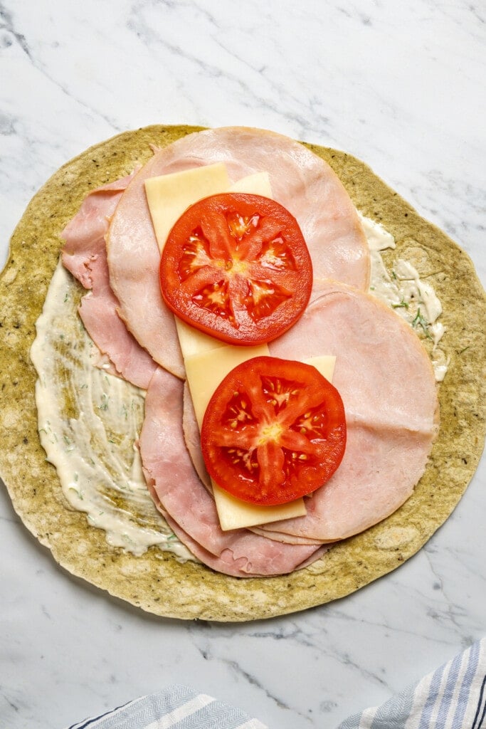 Adding tomatoes to a wrap spread with dijon-dill mayo and filled with meats and cheeses.