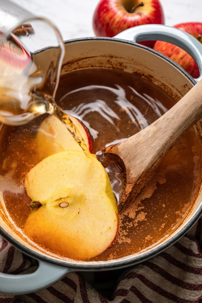 Adding rum to spiced apple cider in a pot on the stove.