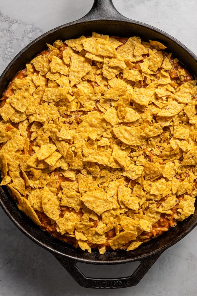 Topping taco casserole with crushed tortilla chips.