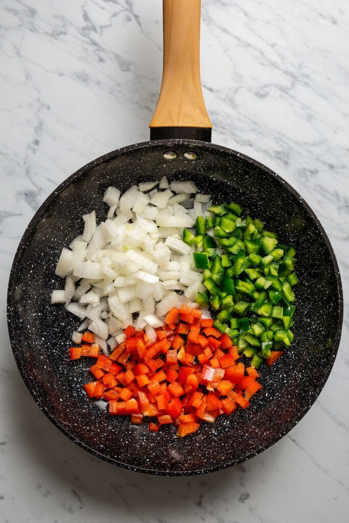 Adding diced onion and red and green bell peppers to a pan.