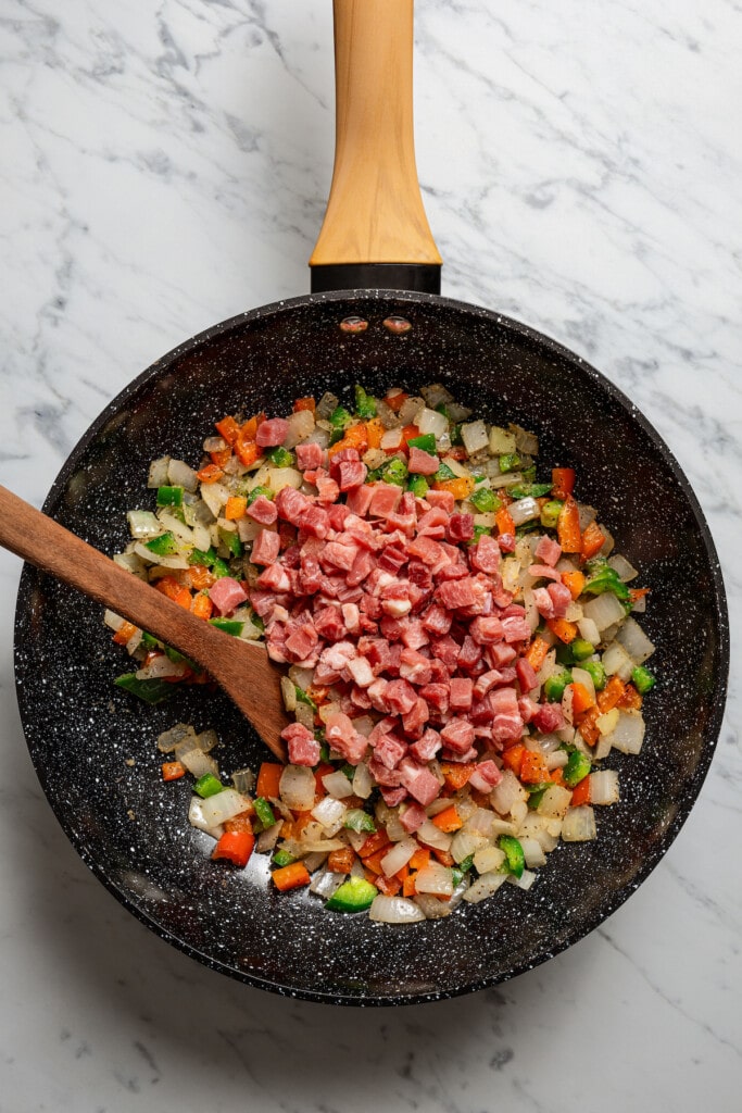 Adding diced ham to a pan full of sauteed veggies.