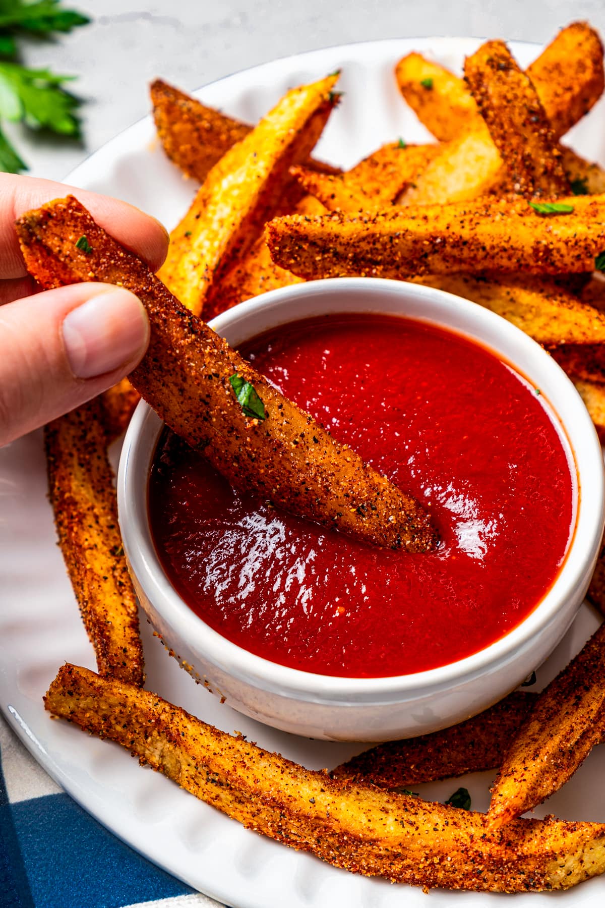 A hand dipping a Cajun fry in ketchup.