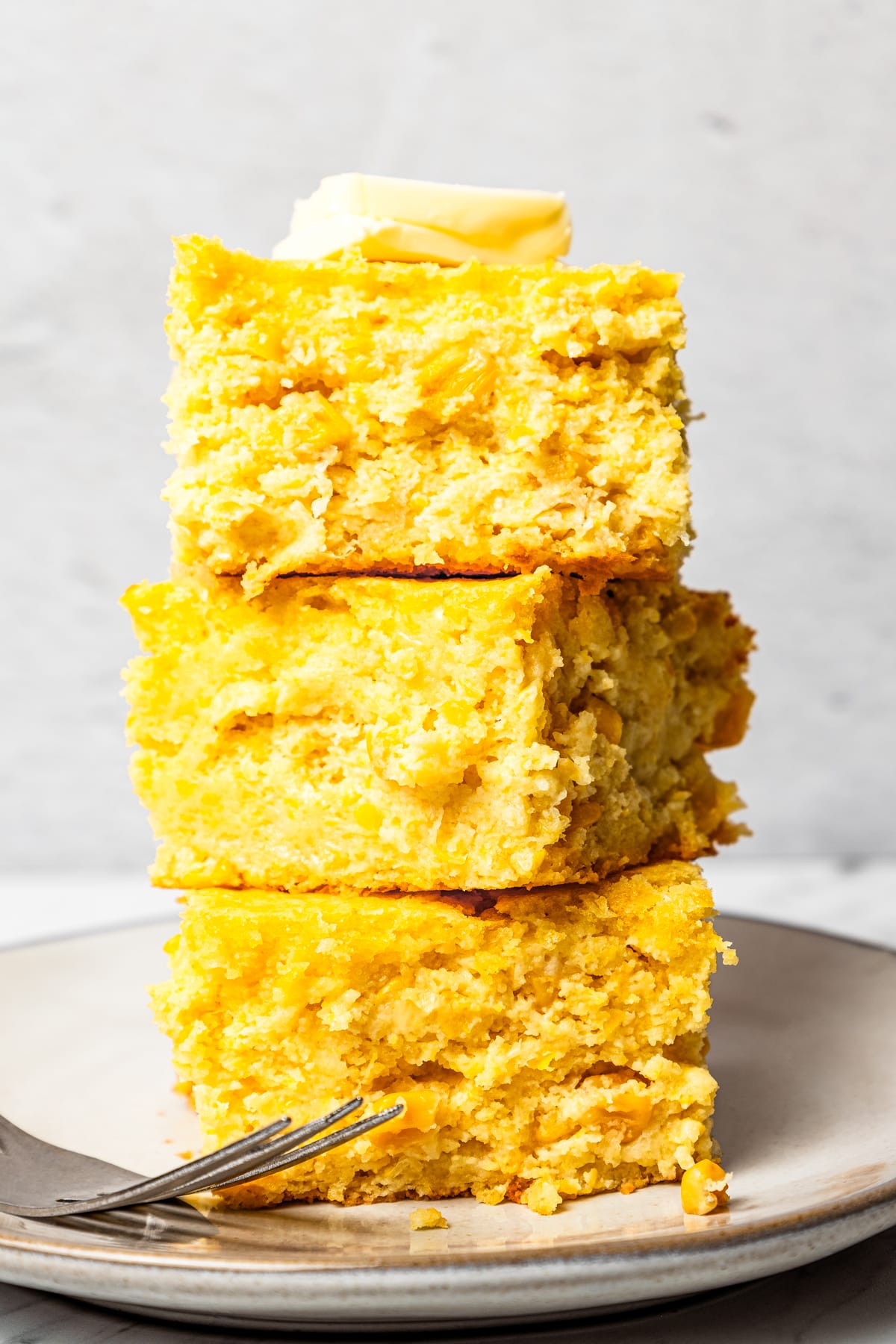 Three pieces of cornbread stacked on top of one another with a pad of butter on top.