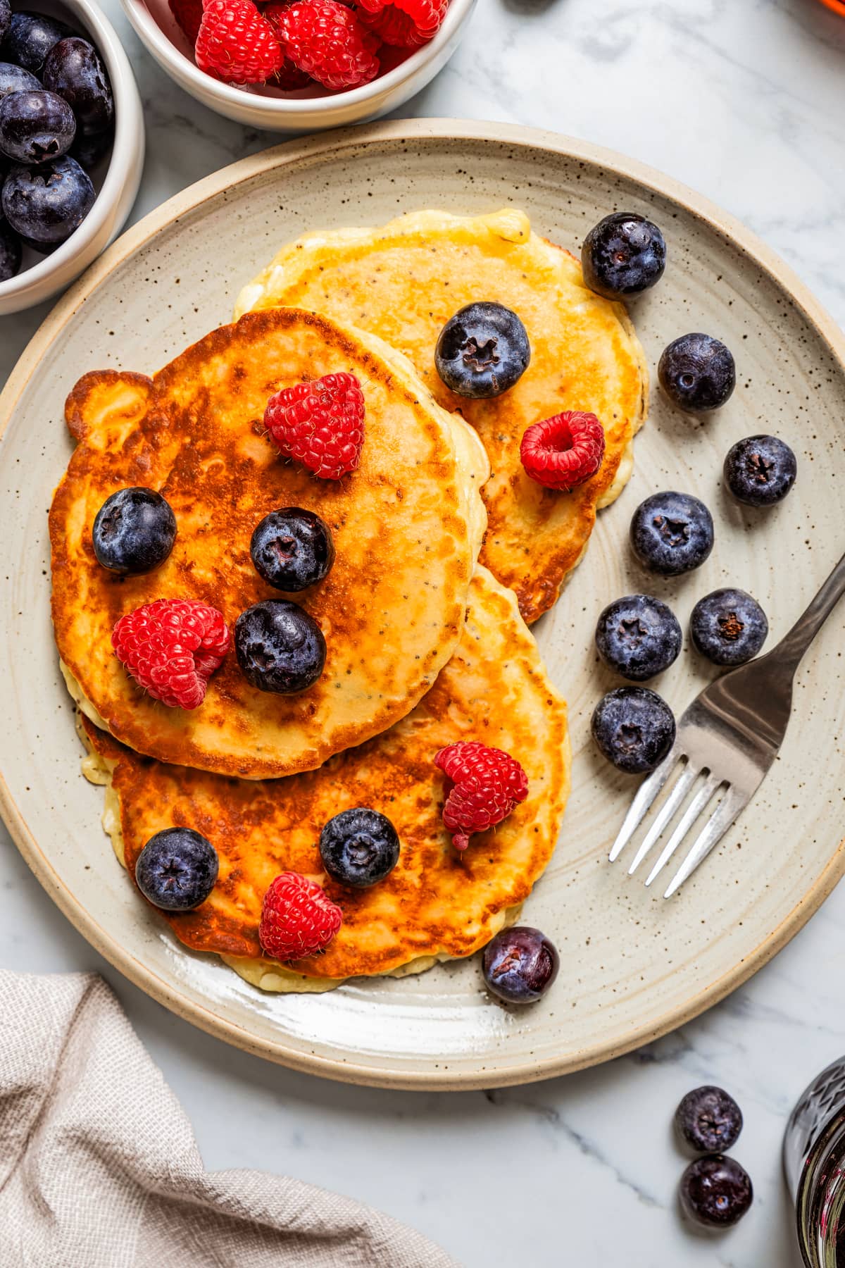 Three pancakes served on a plate and topped with blueberries and raspberries.