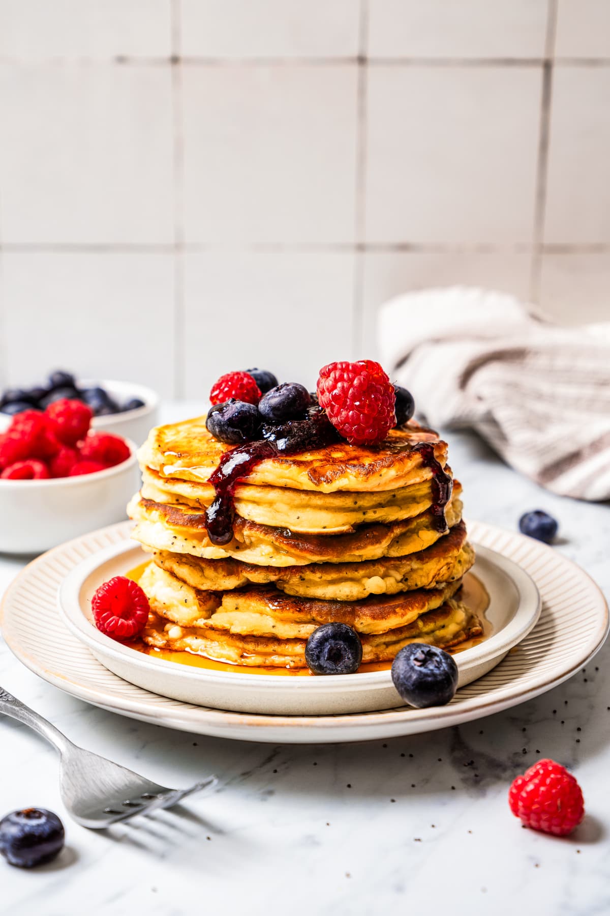 Enjoy these sweet, soft, and deliciously fluffy Cottage Cheese Pancakes, a protein-packed breakfast treat flavored with zesty lemon for a refreshing twist. Cottage cheese pancakes stacked on a white plate and topped with raspberries and blueberries.