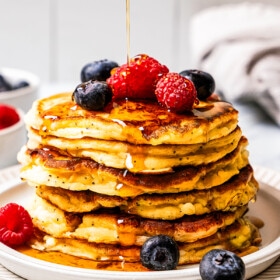 Pouring maple syrup over a stack of cottage cheese pancakes.