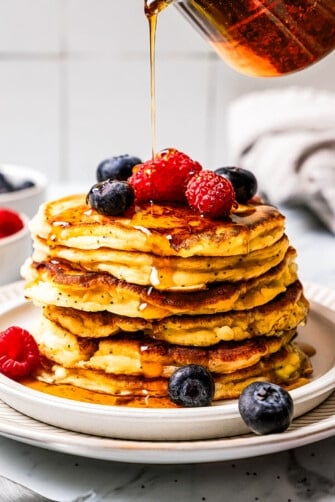 Pouring maple syrup over a stack of cottage cheese pancakes.