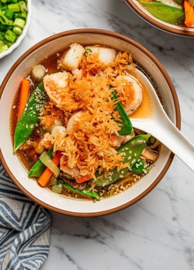 Overhead image of a soup bowl filled with broth, scallops, shrimp, and veggies, and topped with fried rice.