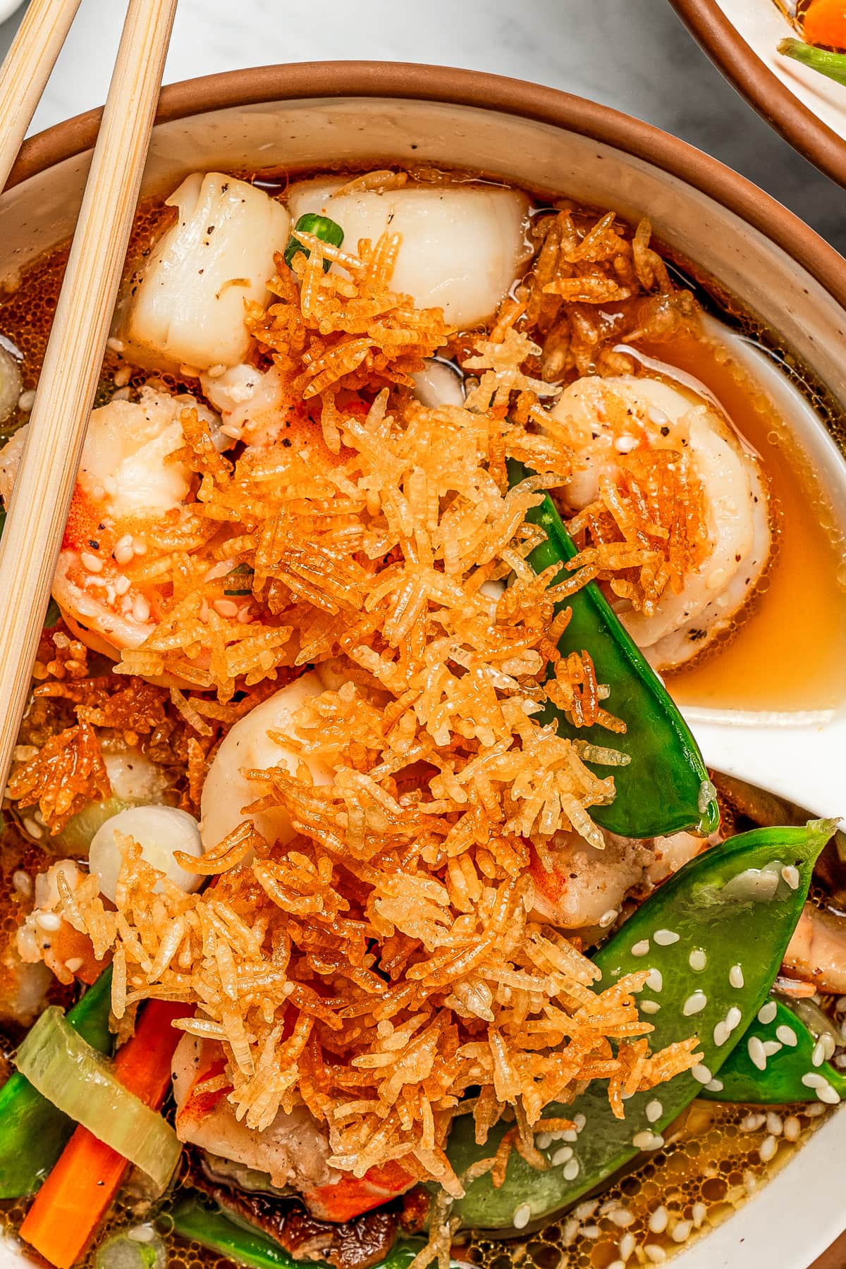 Close up image of fried rice atop a bowl of soup with scallops and veggies.