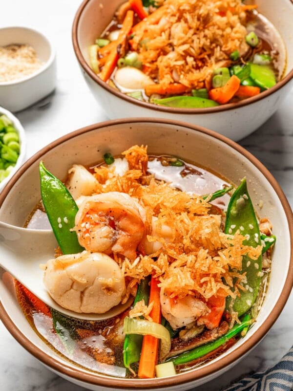 Photo of two bowls filled with Sizzling Rice Soup, with a spoon taking a portion of soup from one of the bowls.