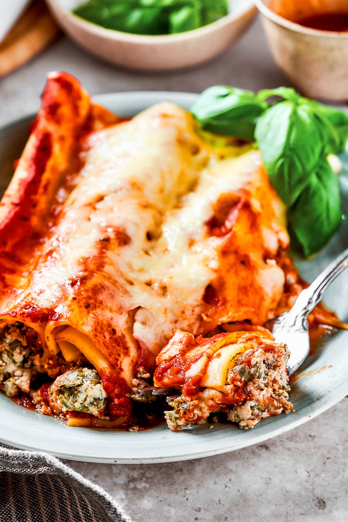 Stuffed manicotti served on a dinner plate with a fork breaking off a bite.
