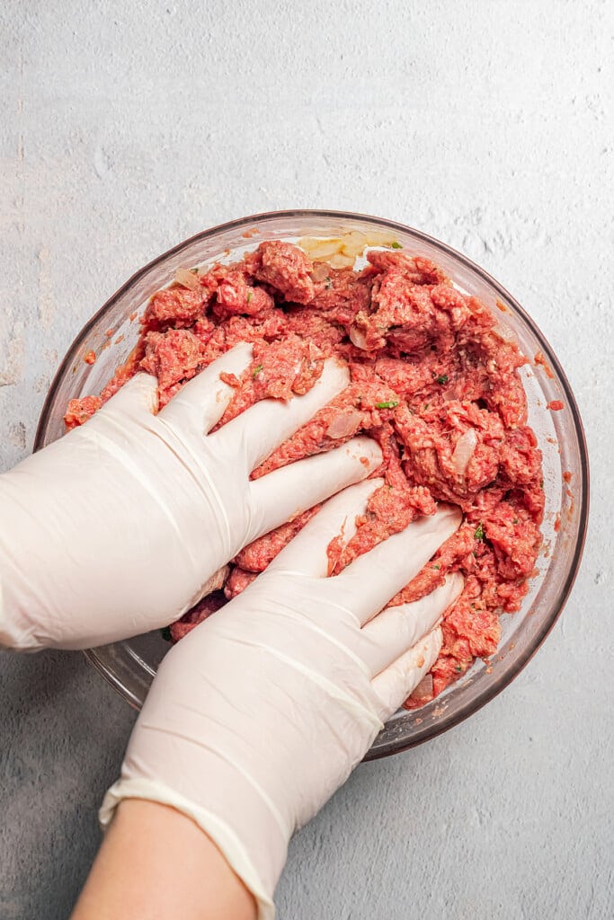 Gloved hands mixing together ingredients for meatloaf.