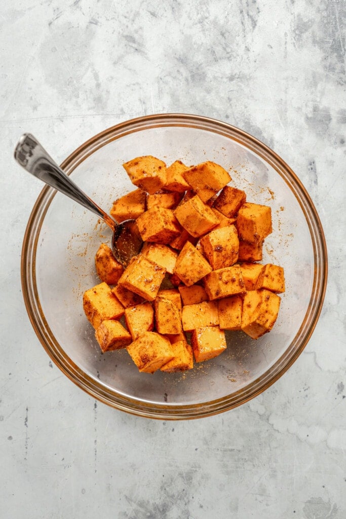 Tossing cubes sweet potatoes with olive oil, salt, garlic powder, smoked paprika, and cumin.