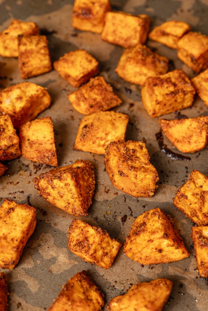 Cumin roasted sweet potato cubes on a baking sheet lined with parchment paper.