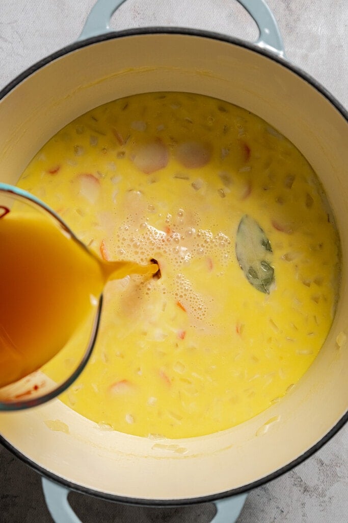 Pouring chicken stock into a soup pot with sauteed veggies and milk.