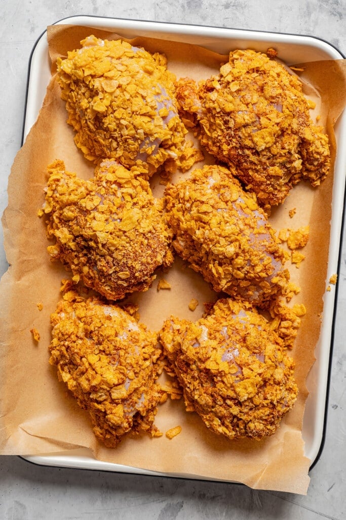 Chicken thighs coated with cornflakes ready to be baked.