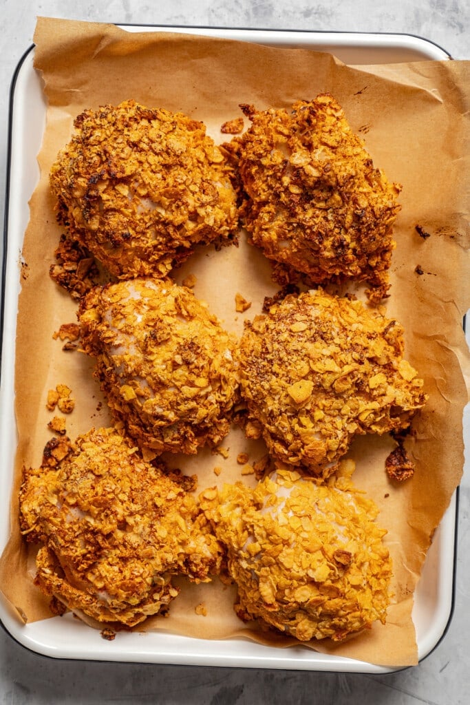 Cornflake crusted chicken thighs in a baking dish lined with parchment paper.
