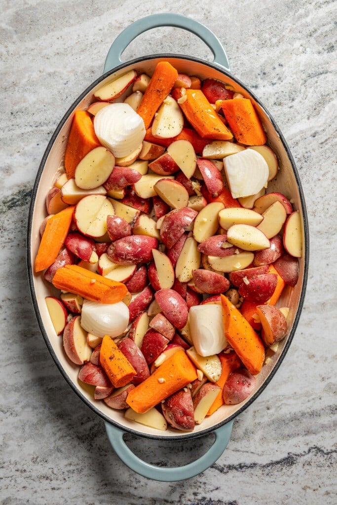 Onions, potatoes, carrots, and garlic in a baking dish.
