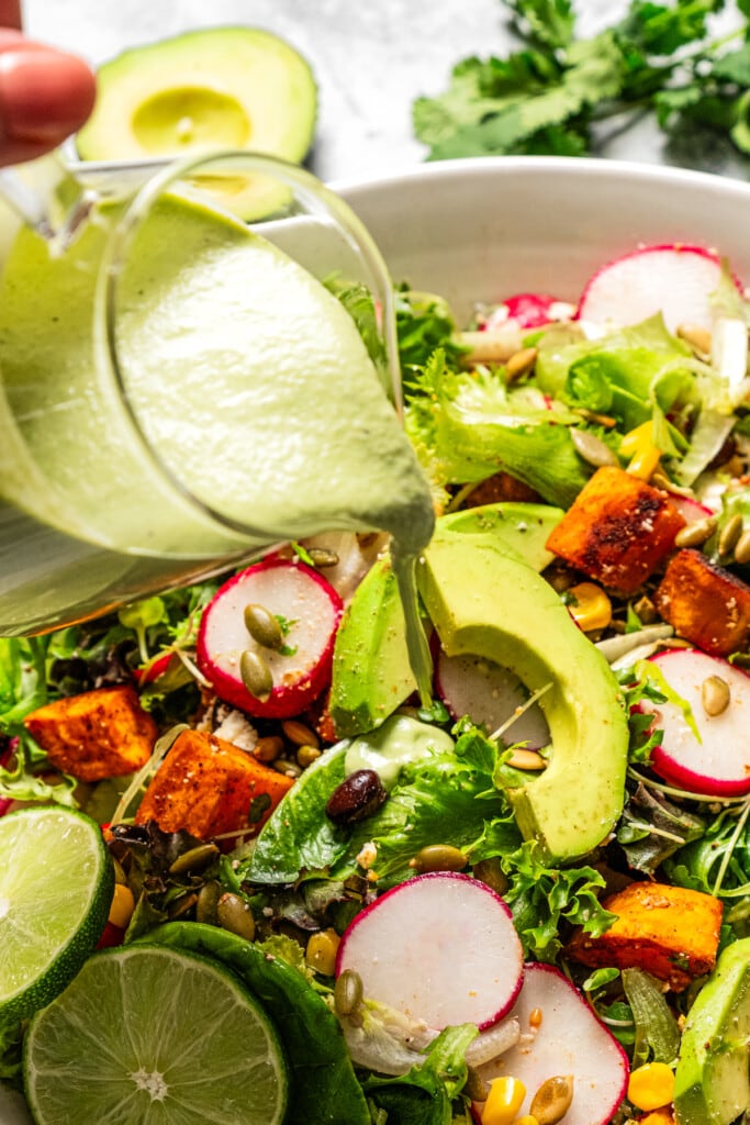 Pouring avocado lime ranch dressing over a salad.