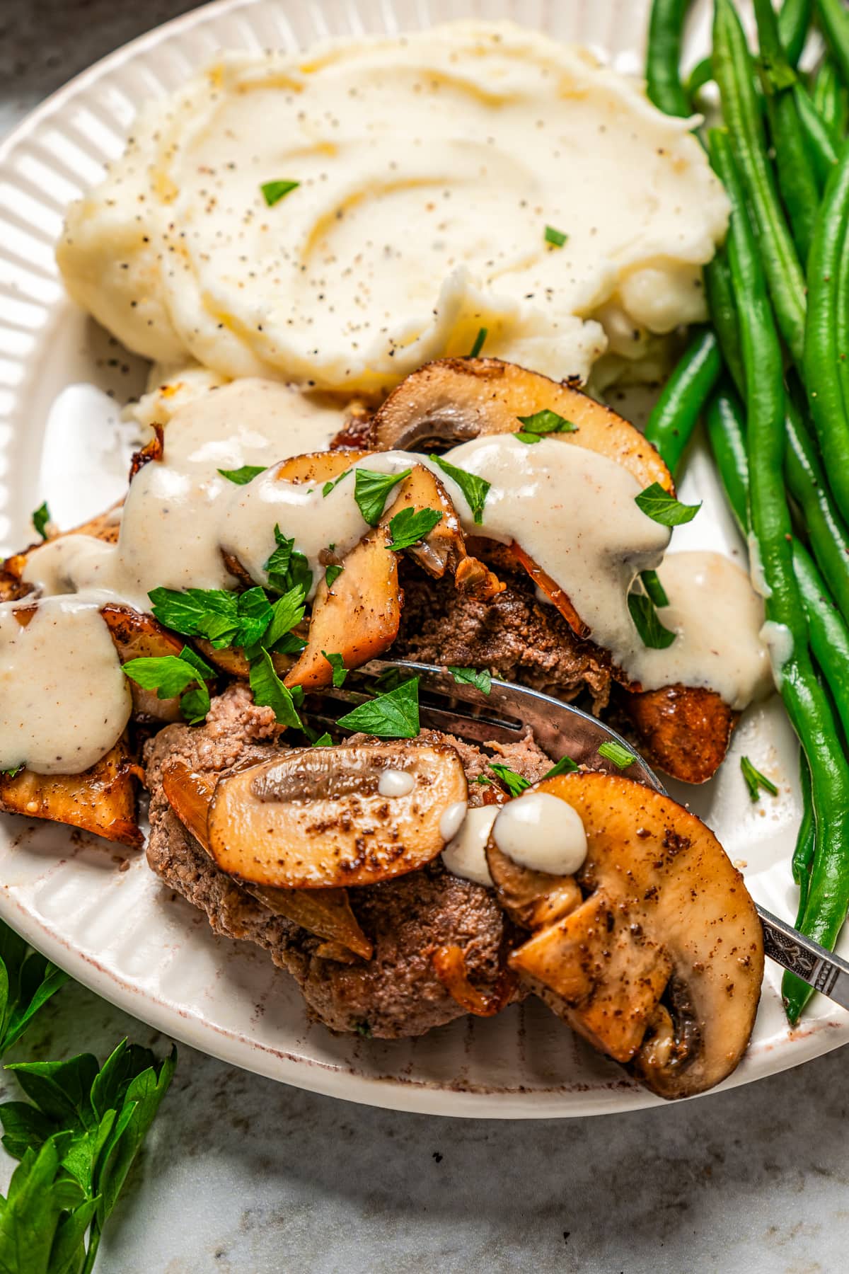 Chopped steak on a plate with mashed potatoes and green beans.