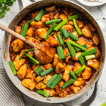 Mongolian chicken in a pan near a bowl of rice and some limes.