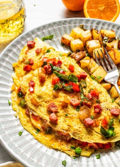 A Western omelette on a plate with breakfast potatoes and a fork.