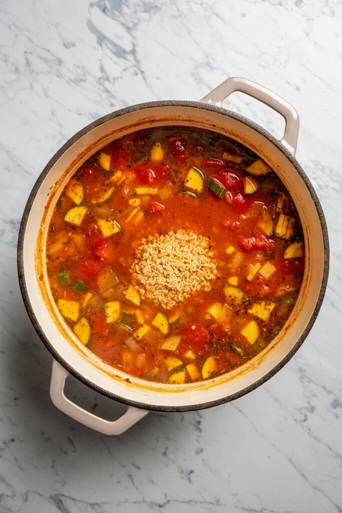 Adding alphabet pasta to a pot of tomato and veggie soup.