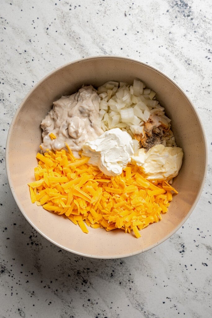Adding hash browns, onion, cream of chicken, butter, sour cream, mayo, salt, pepper, garlic powder, and cheddar cheese to a mixing bowl.
