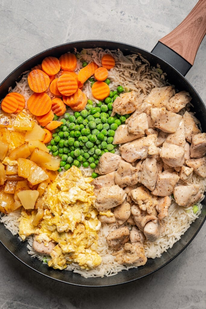 Adding browned chicken, seared pineapple, cooked egg, and frozen veggies to fried rice.