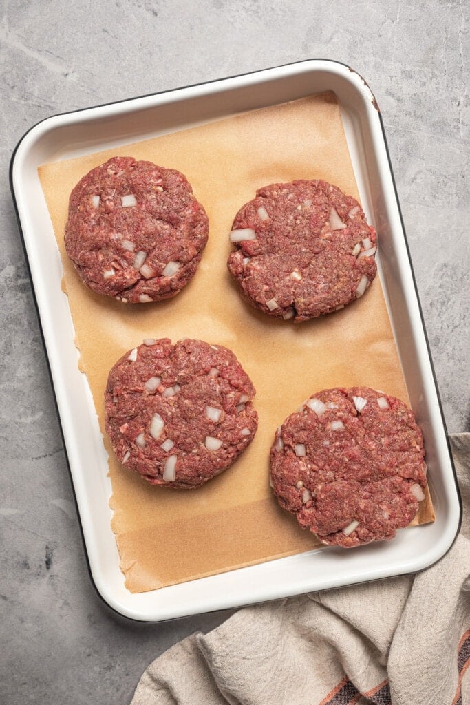 Uncooked burger patties in a baking dish.