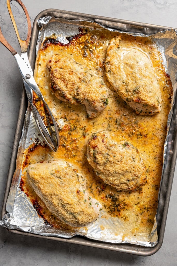 Italian dressing chicken and serving tongs on a baking sheet lined with aluminum foil.