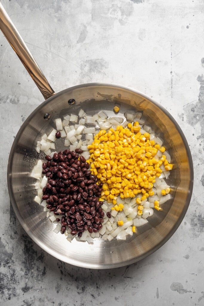 Adding black beans and corn to a pan with sauteed onions.