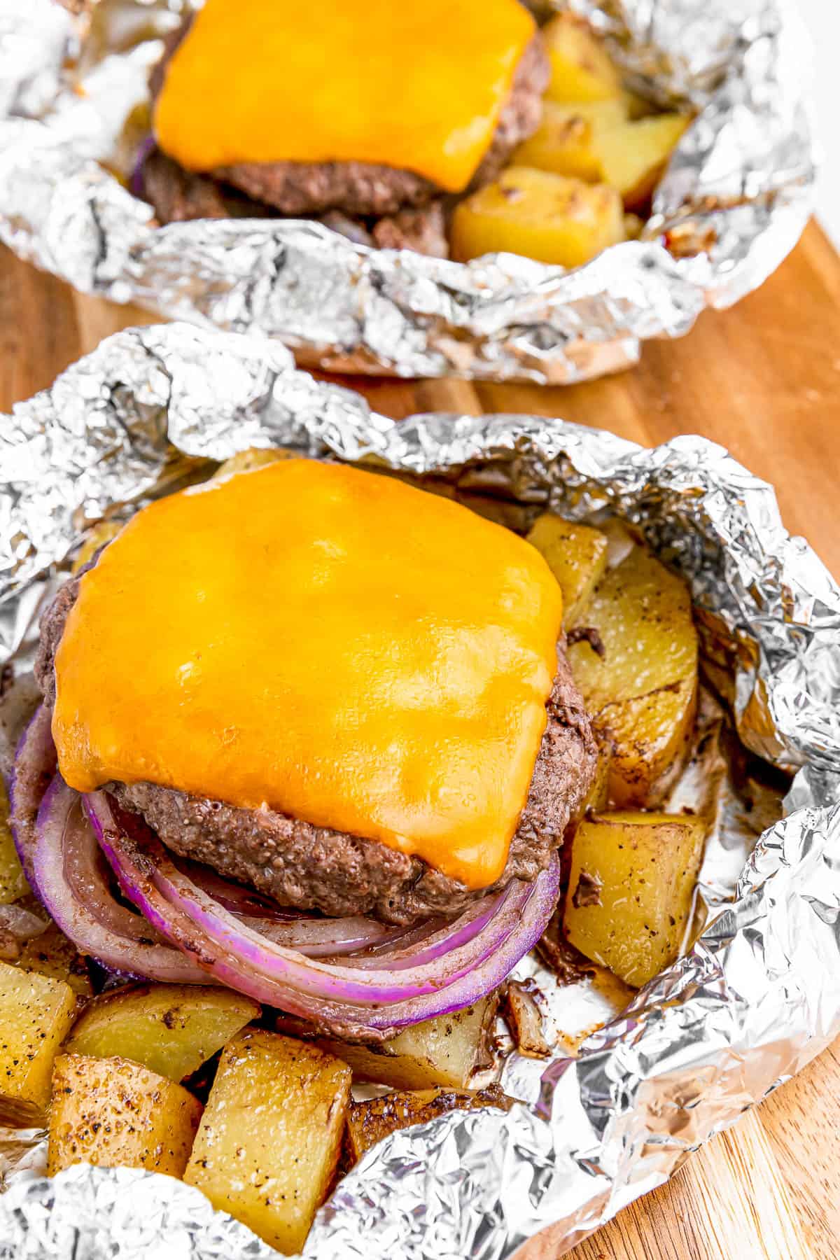 Diced potatoes, burger patty, cheese, and onions arranged on a piece of foil.